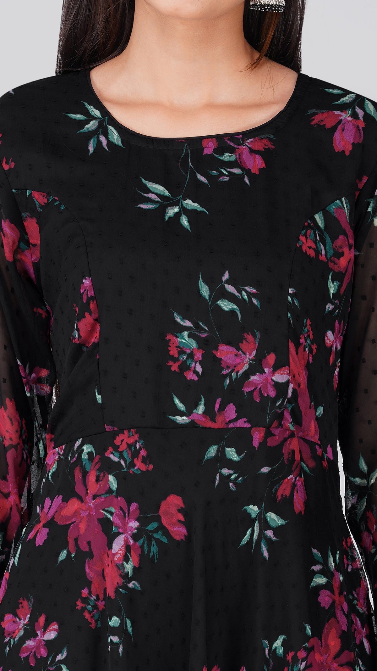 A close-up of a black long-sleeve dress with a vibrant floral print in pink, red, and green, featuring a subtle dotted texture.