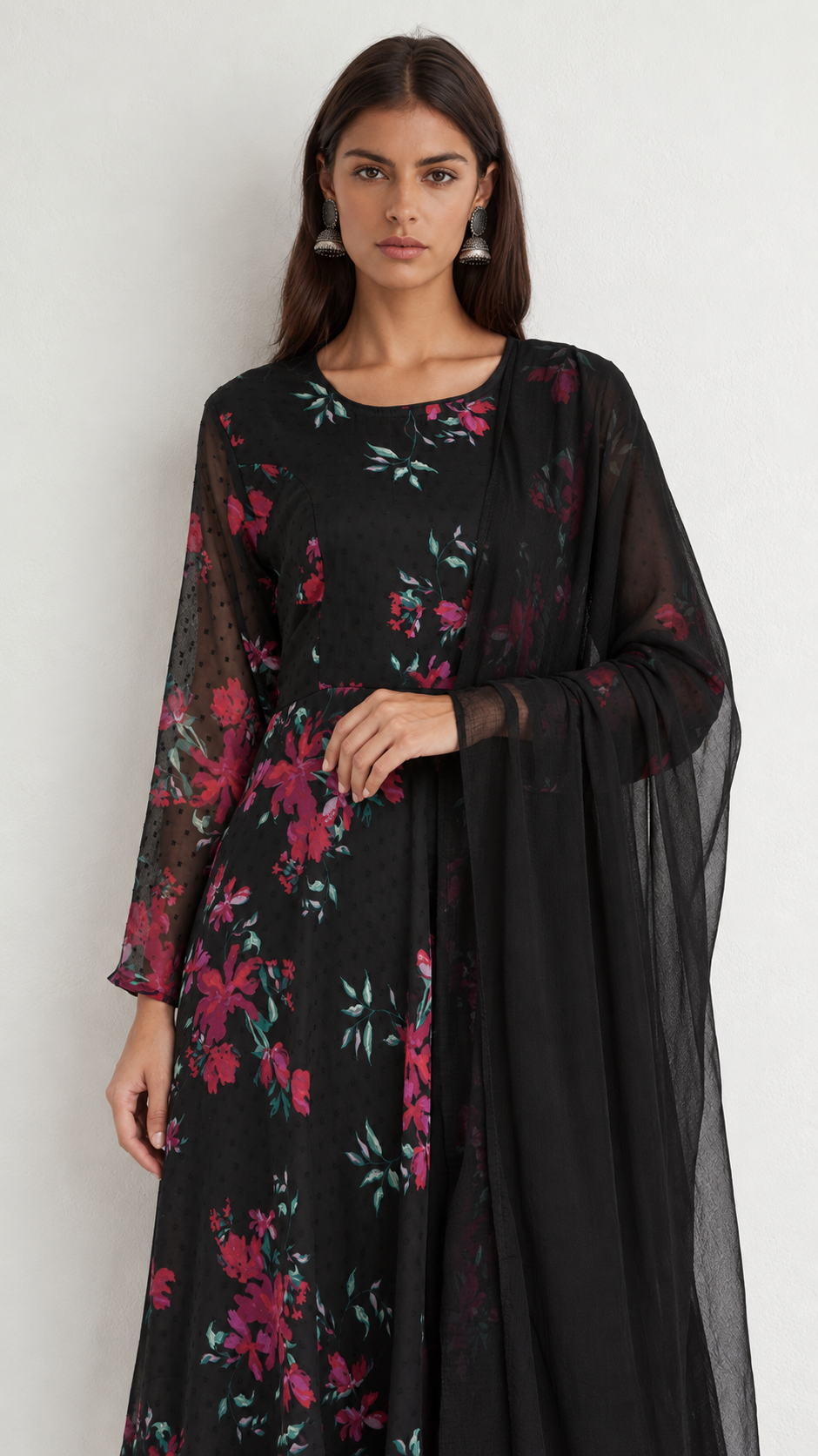 A woman modeling a black long-sleeve kurta with a vibrant pink and green floral print, paired with a matching sheer black dupatta, against a plain light gray background.