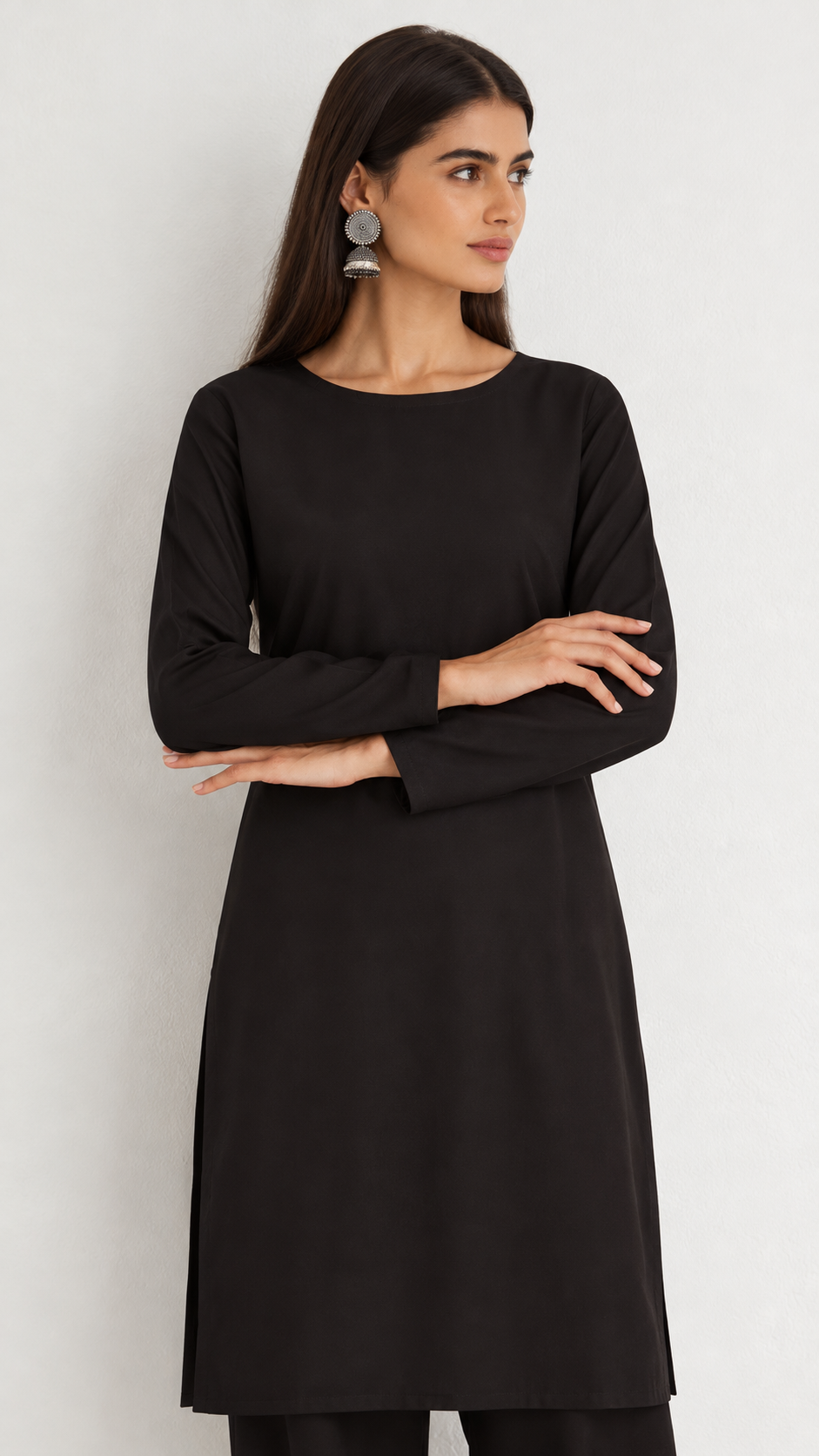 A woman modeling a solid black long-sleeve tunic dress with a boat neckline, posed against a neutral light gray background.