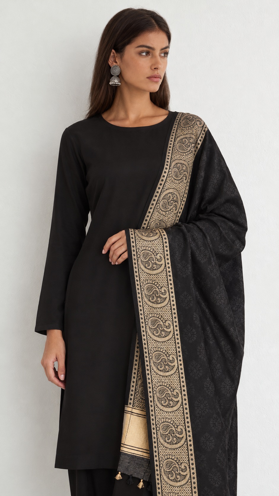 A woman modeling a black long-sleeve kurta with a black dupatta featuring a wide beige and gold paisley border, set against a plain light gray background.