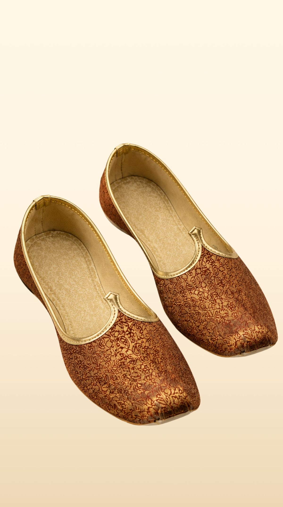 A pair of metallic bronze-brown traditional Indian flat shoes with gold trim, displayed on a light beige gradient background.
