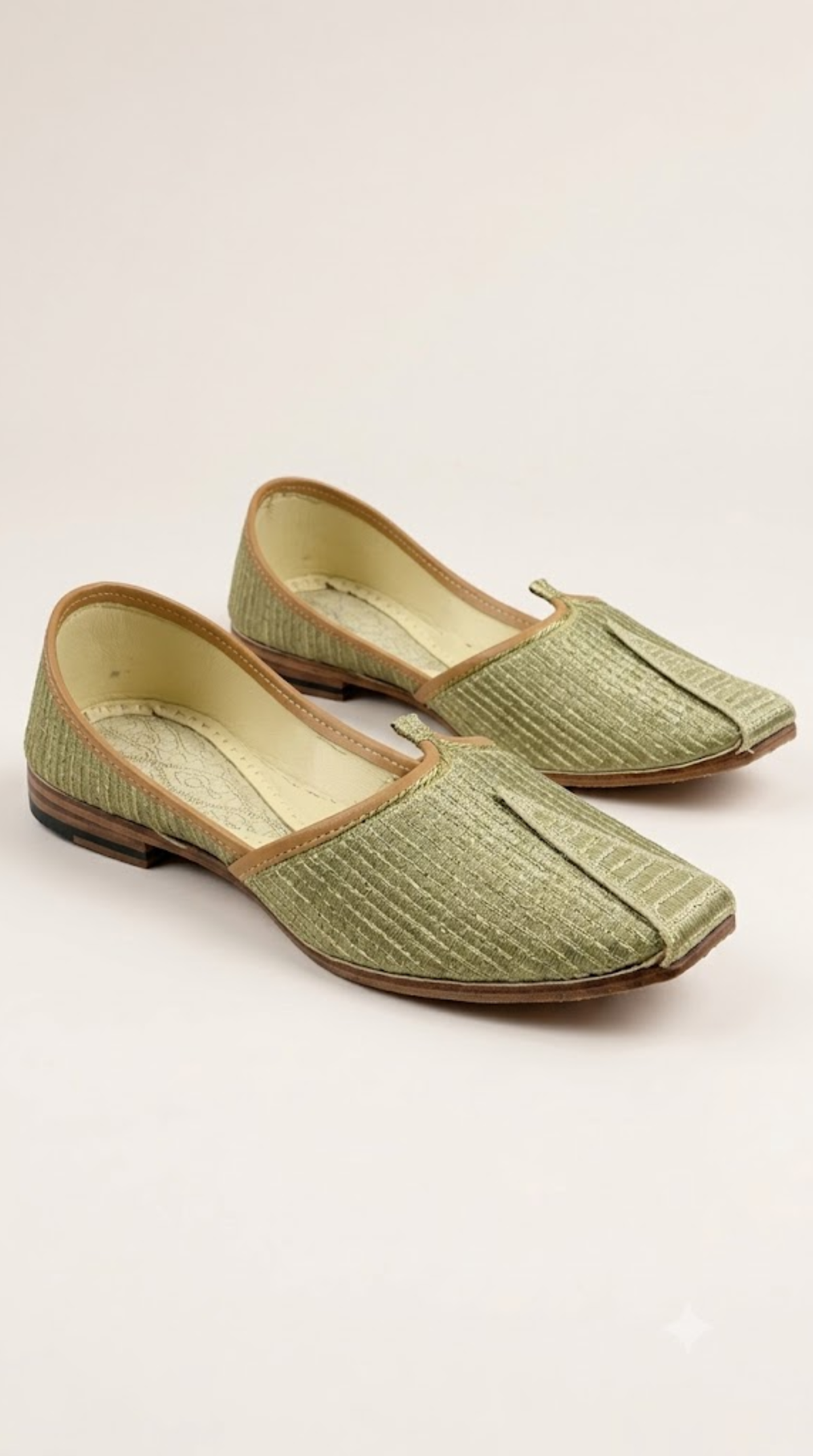 A pair of light olive green textured traditional flat shoes with tan trim, photographed on a clean off-white background.