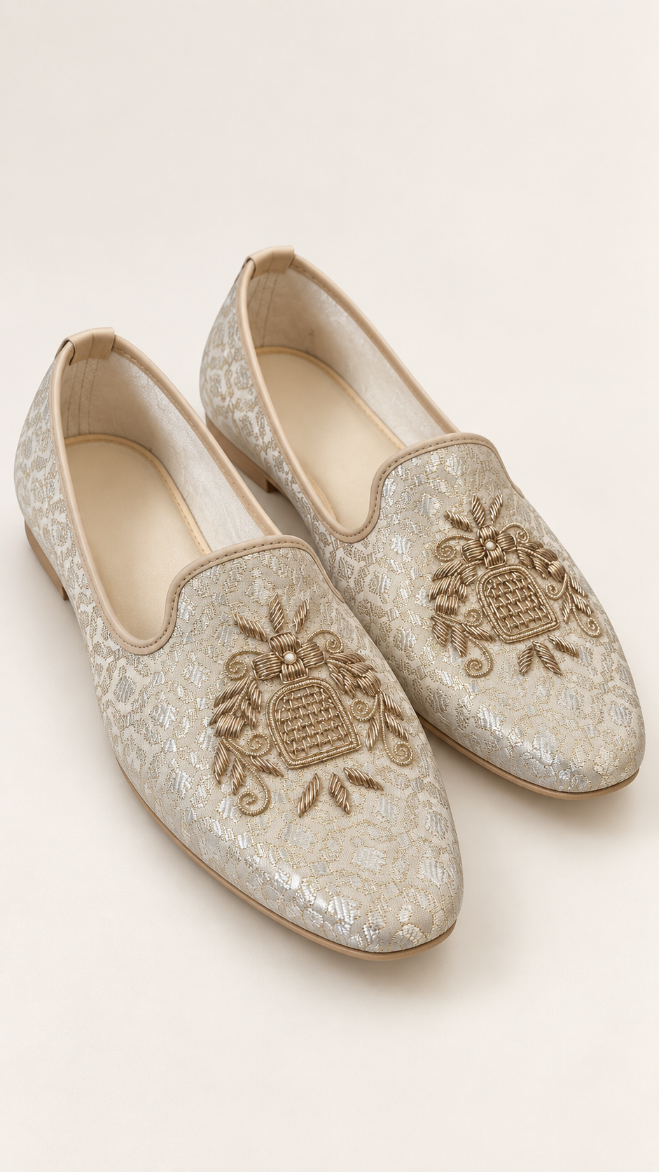 Mens slip-on loafers in a textured champagne beige fabric with intricate gold embroidery on the toe, displayed on a light cream background.
