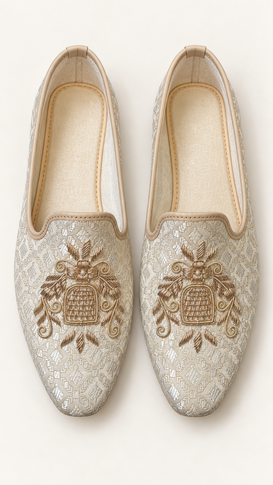 A pair of slip-on Men's Brocade loafers in achampagne beige fabric with intricate gold embroidery on the toe area, shown from a top-down view on a light cream background