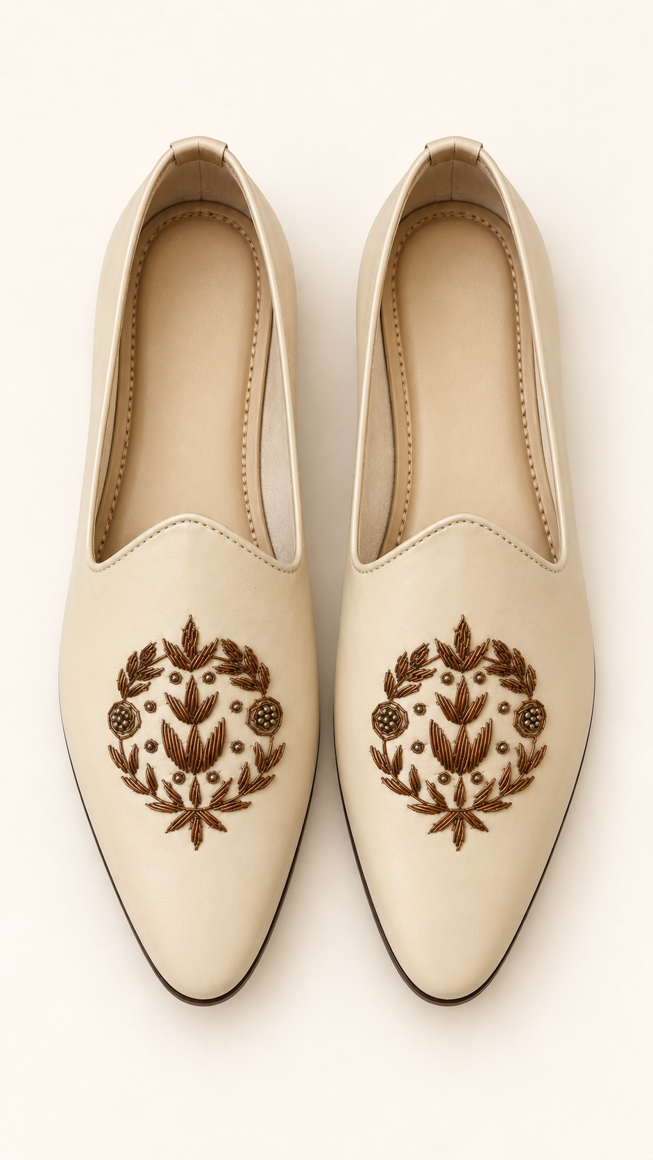 A pair of cream-colored pointed-toe slip-on shoes with brown floral and leaf embroidery on the front, displayed against a light cream background.