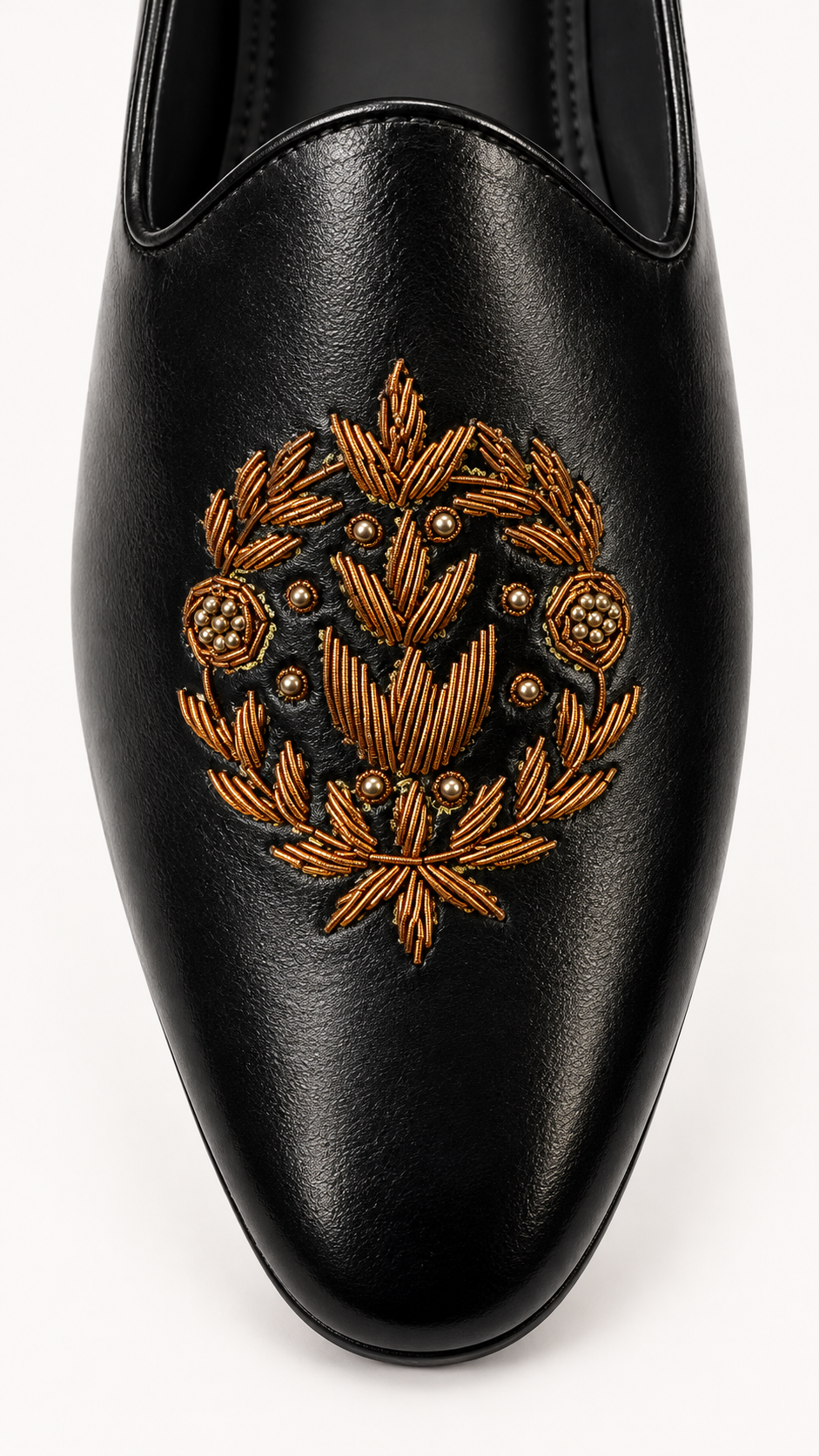 A close-up of a black leather slip-on shoe featuring an ornate gold embroidered wreath design on the toe box, set against a plain white background.