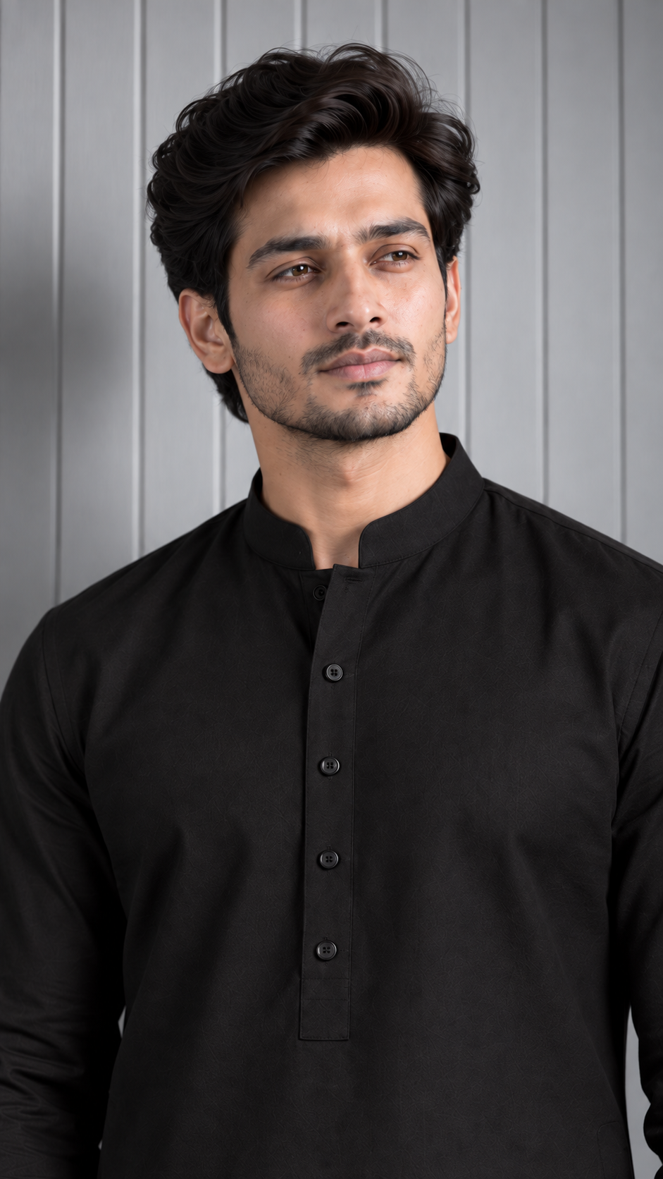 A man wearing a black long-sleeve mandarin-neck kurta with a button placket, standing against a gray paneled wall.