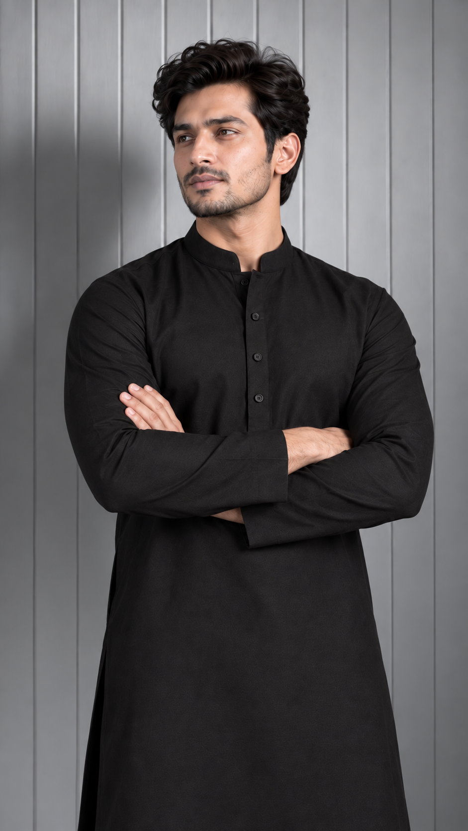 A man wearing a black long-sleeve kurta with a mandarin collar and button placket, standing with arms crossed against a gray paneled background.