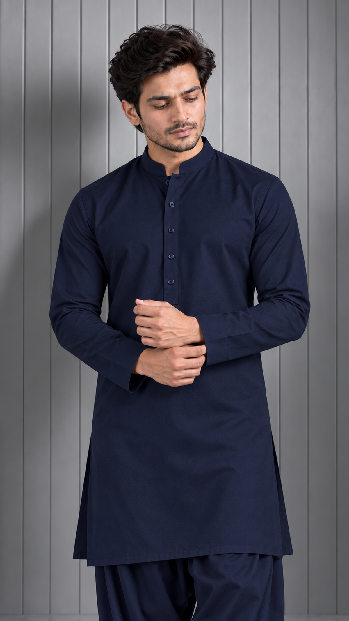 A man wearing a dark navy blue long-sleeve kurta with a mandarin collar and matching pants, standing against a gray paneled background.