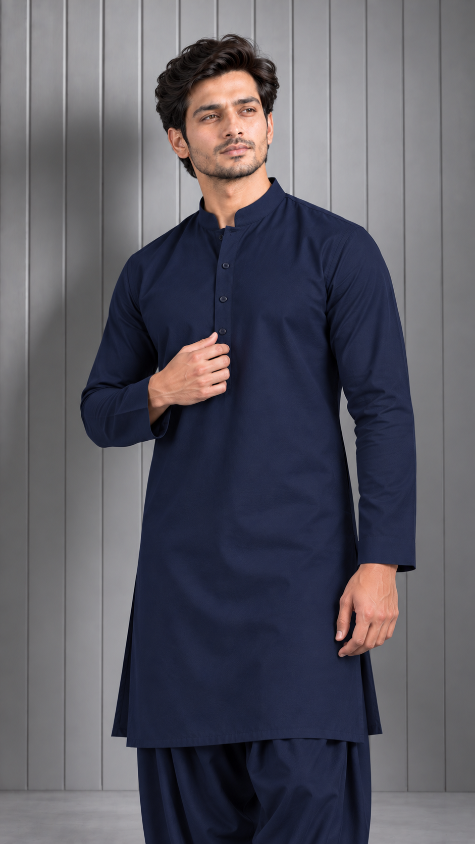 A man modeling a dark navy blue long kurta with a mandarin collar and button placket, paired with matching navy pants, set against a gray paneled studio background.