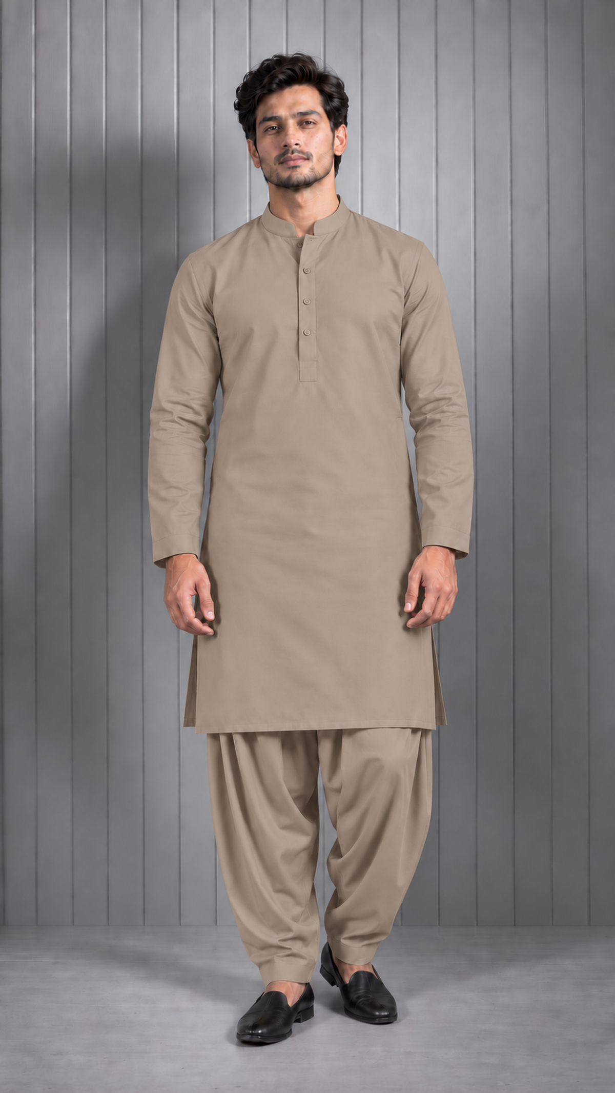 A man modeling a traditional beige kurta and shalwar set against a gray paneled studio background.