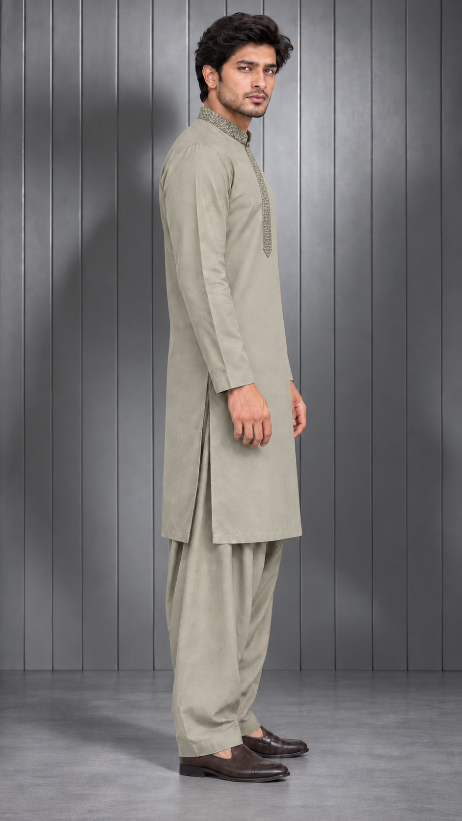 A man modeling a light beige long-sleeve kurta and matching trousers set, standing in profile against a dark gray paneled studio background.