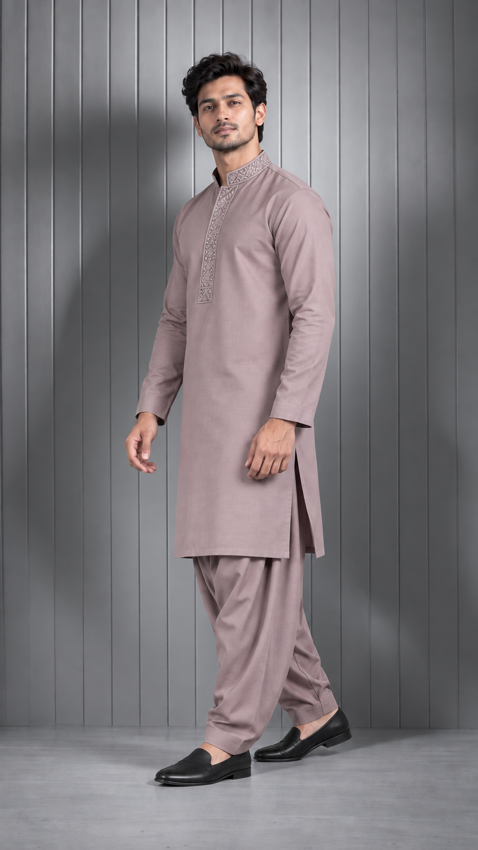 A man modeling a traditional Indian outfit consisting of a long-sleeved kurta and matching trousers in a dusty mauve color, paired with black loafers, set against a gray paneled studio background.