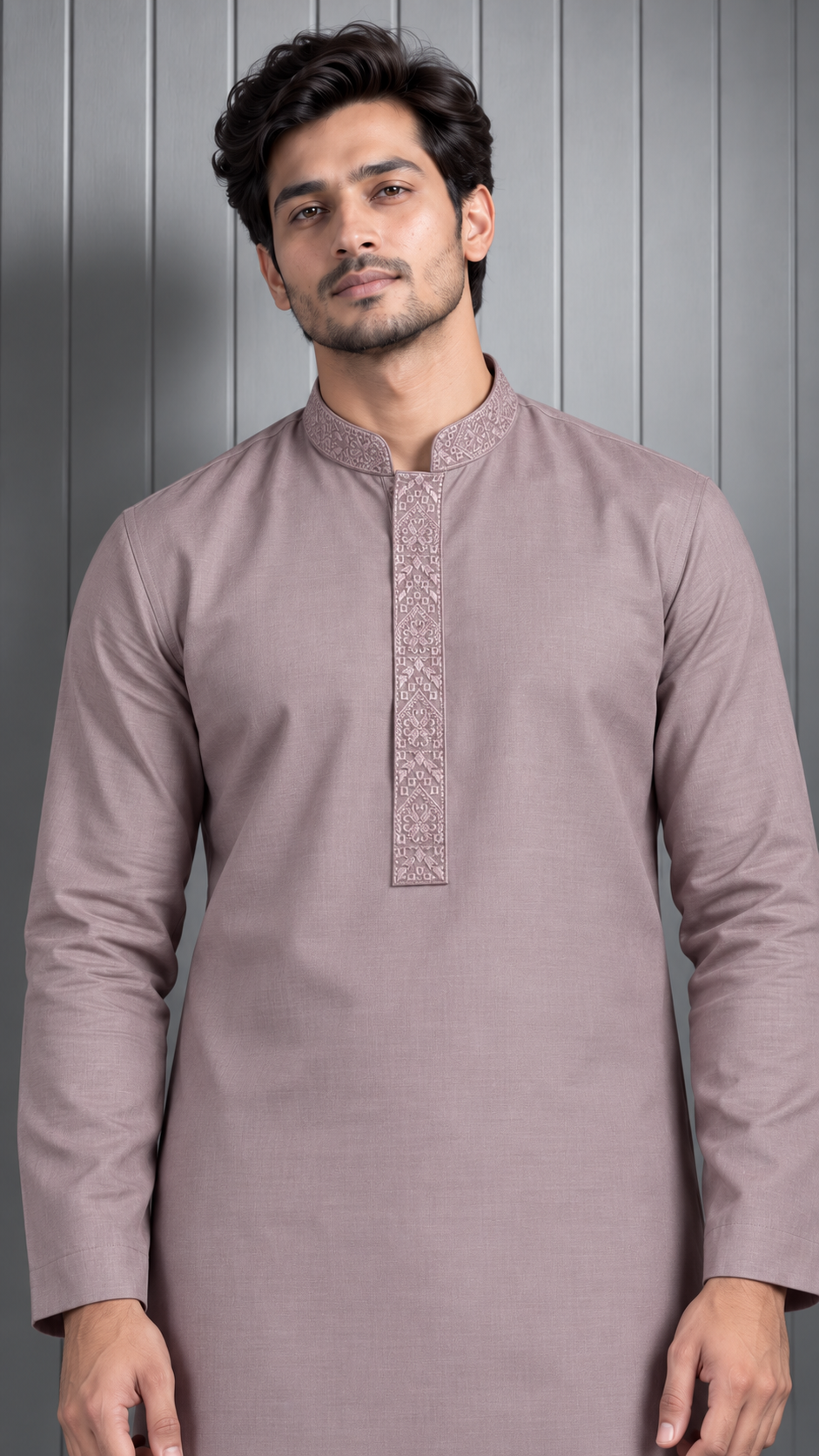 A man wearing a long-sleeve kurta in a dusty mauve color with a textured embroidered neckline, standing against a gray paneled background.