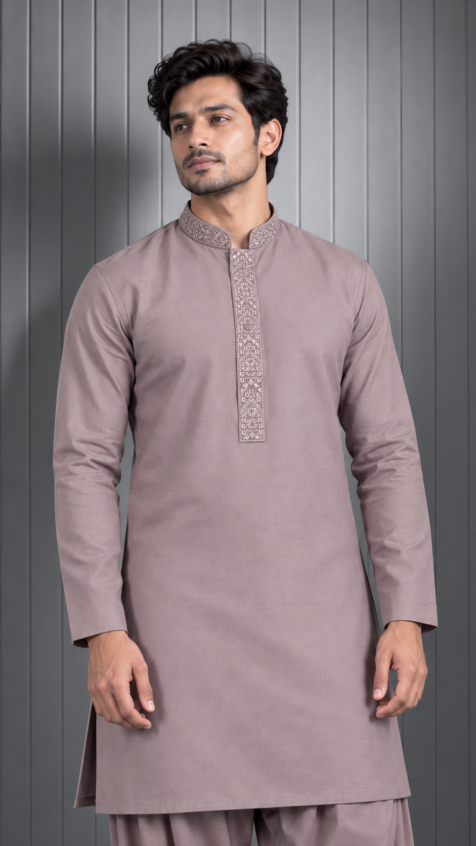 A man wearing a light taupe long-sleeve kurta with a decorative embroidered yoke and matching trousers, standing against a gray paneled background.