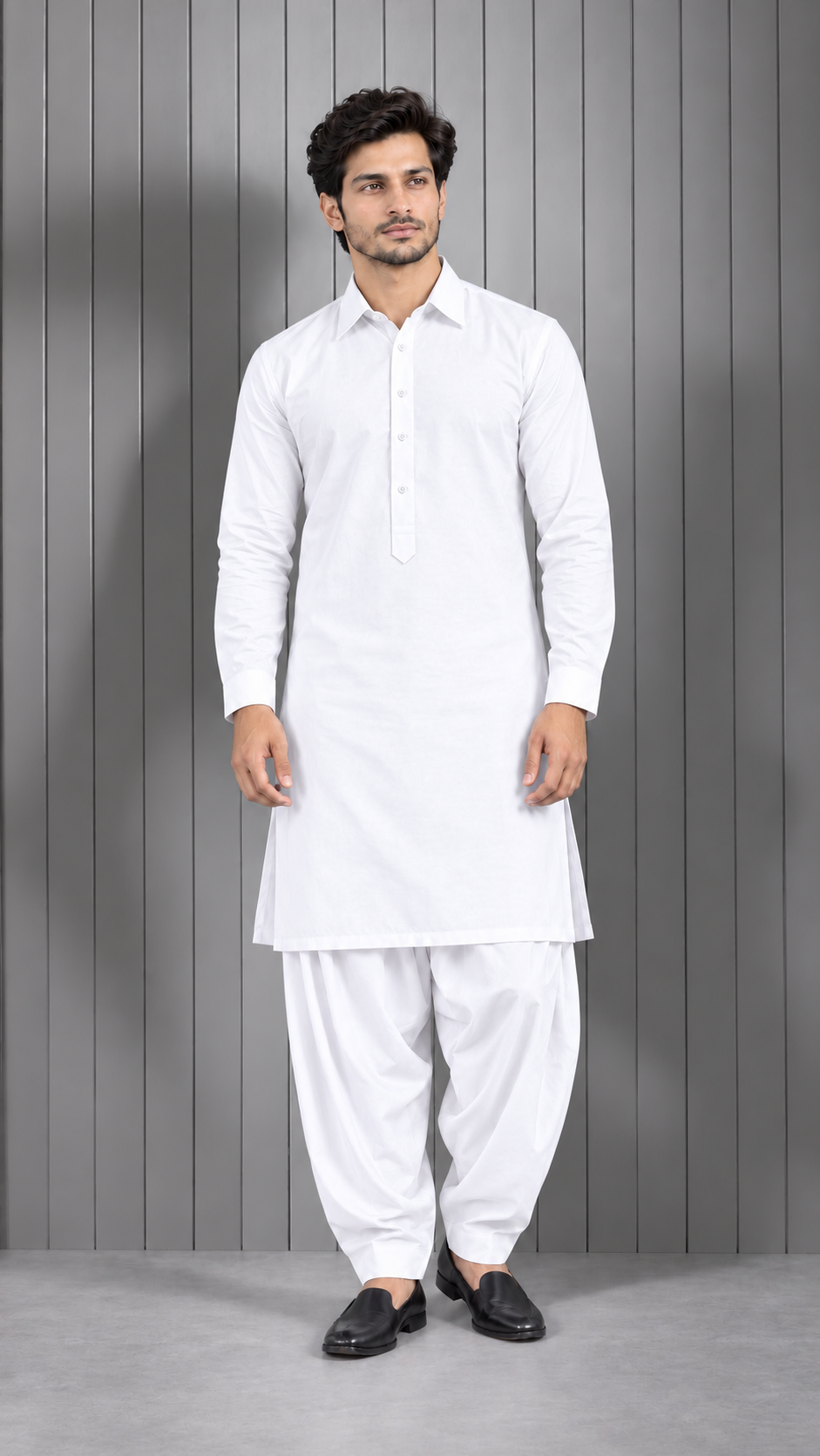 A man modeling a white long-sleeve kurta and white patthar pants set, standing against a gray vertical-paneled studio background.