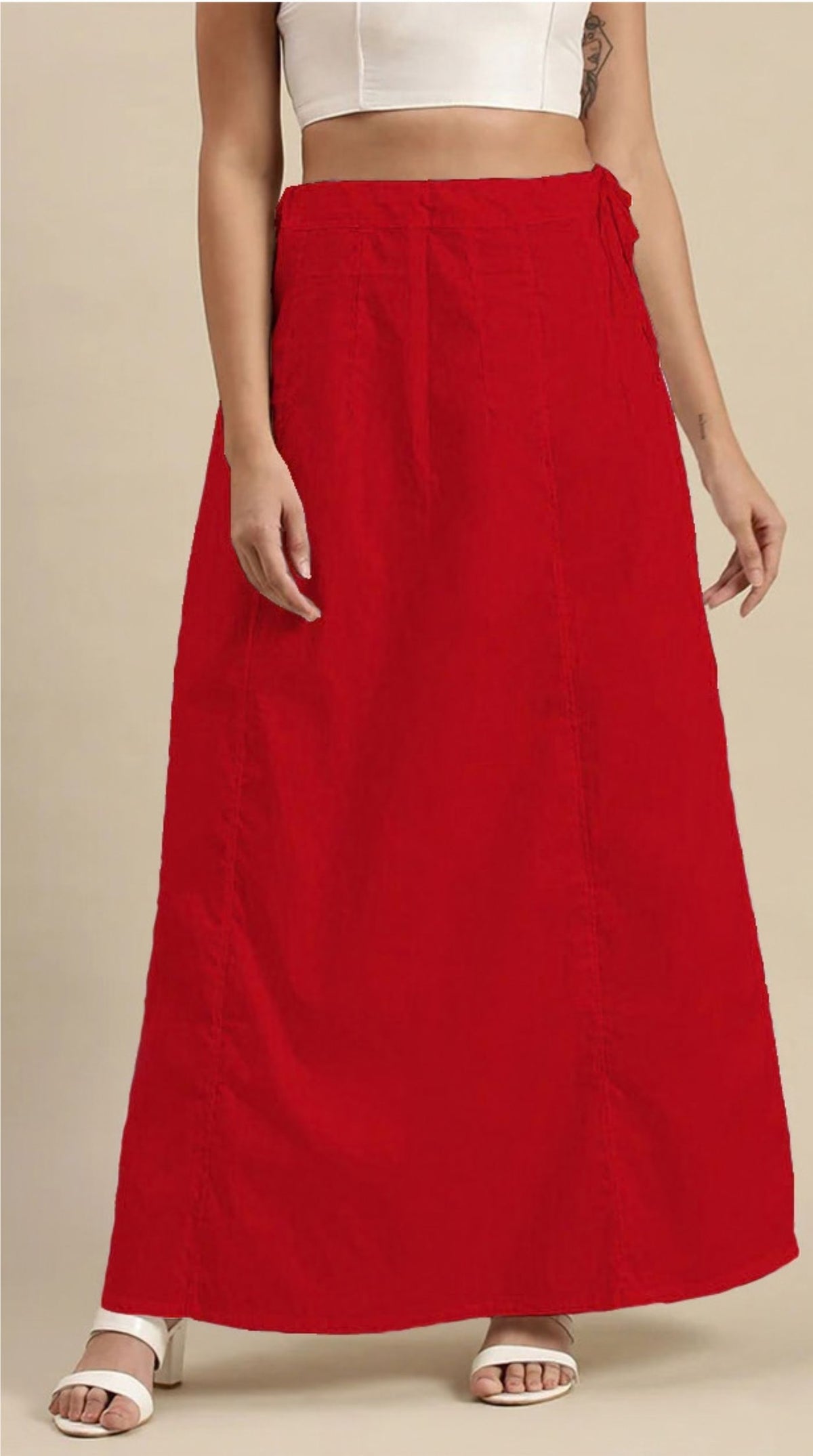 A model wearing a bright red, high-waisted maxi skirt with a side tie, paired with a white crop top and white heeled sandals, set against a plain beige background.