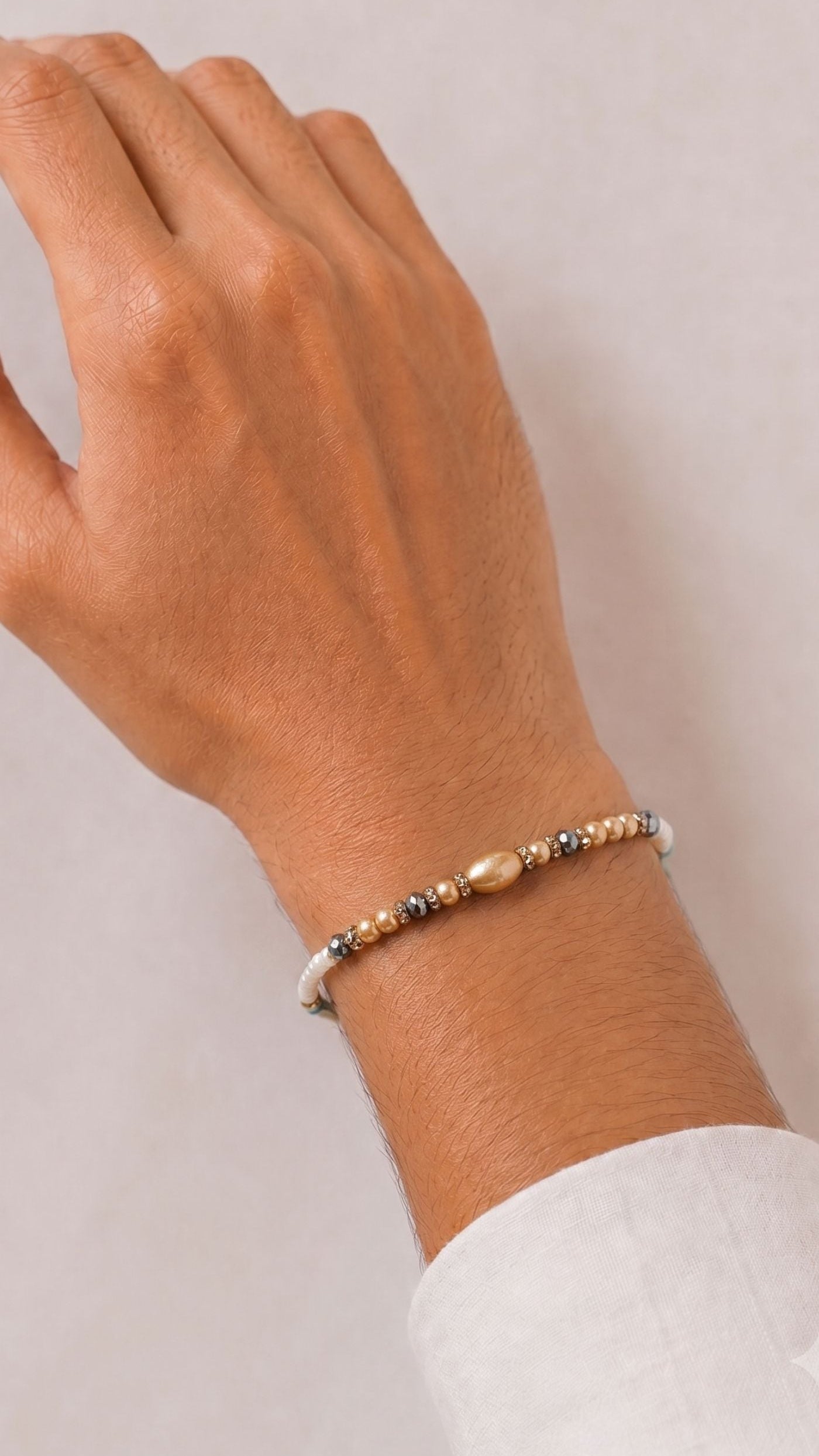 gold and silver beaded rakhi bracelet with white seed beads worn on a man’s wrist – Diya Online UK
