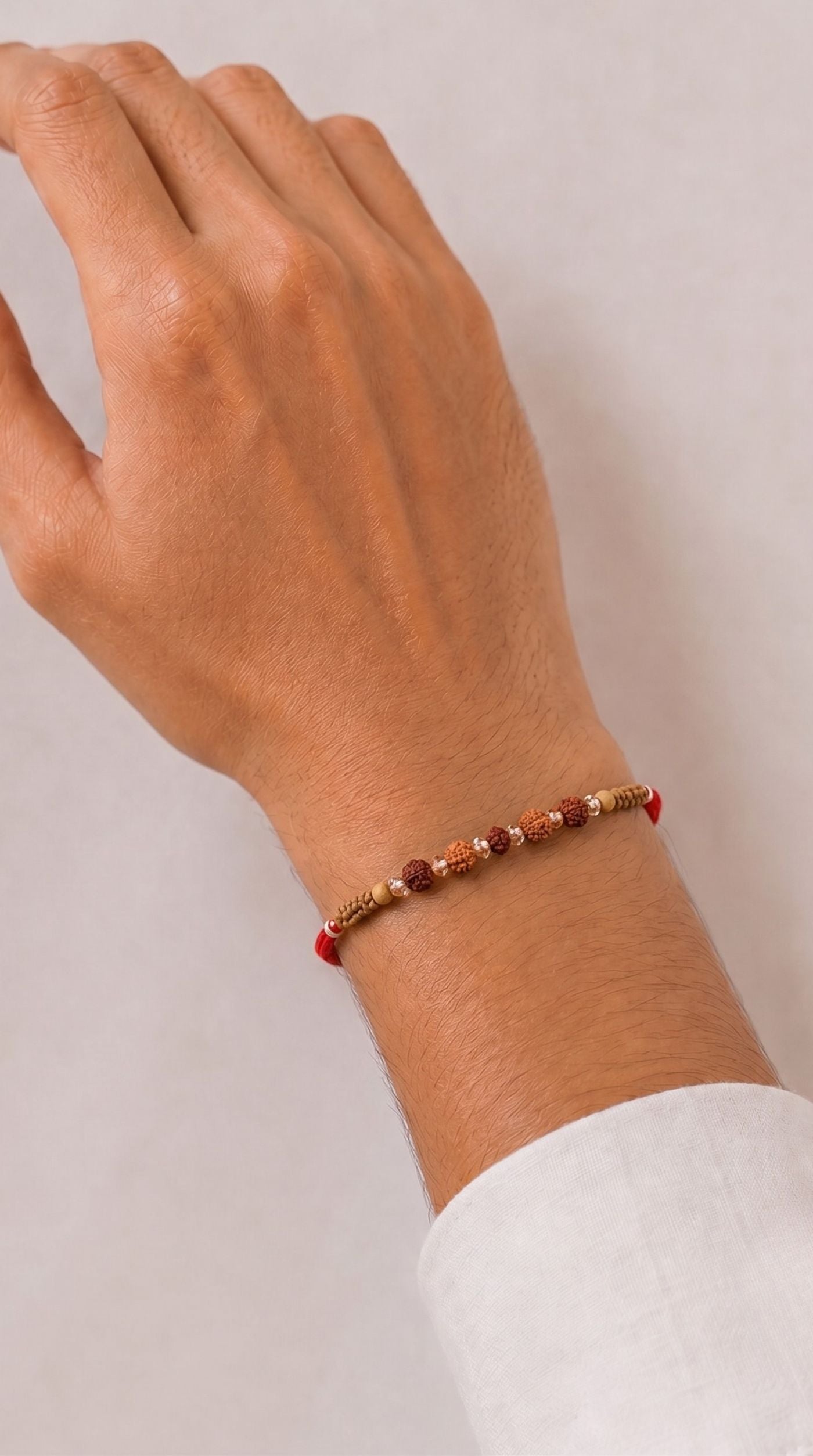 Brown rudraksha-style beaded rakhi with clear crystal beads and red thread worn on a man’s wrist – Diya Online