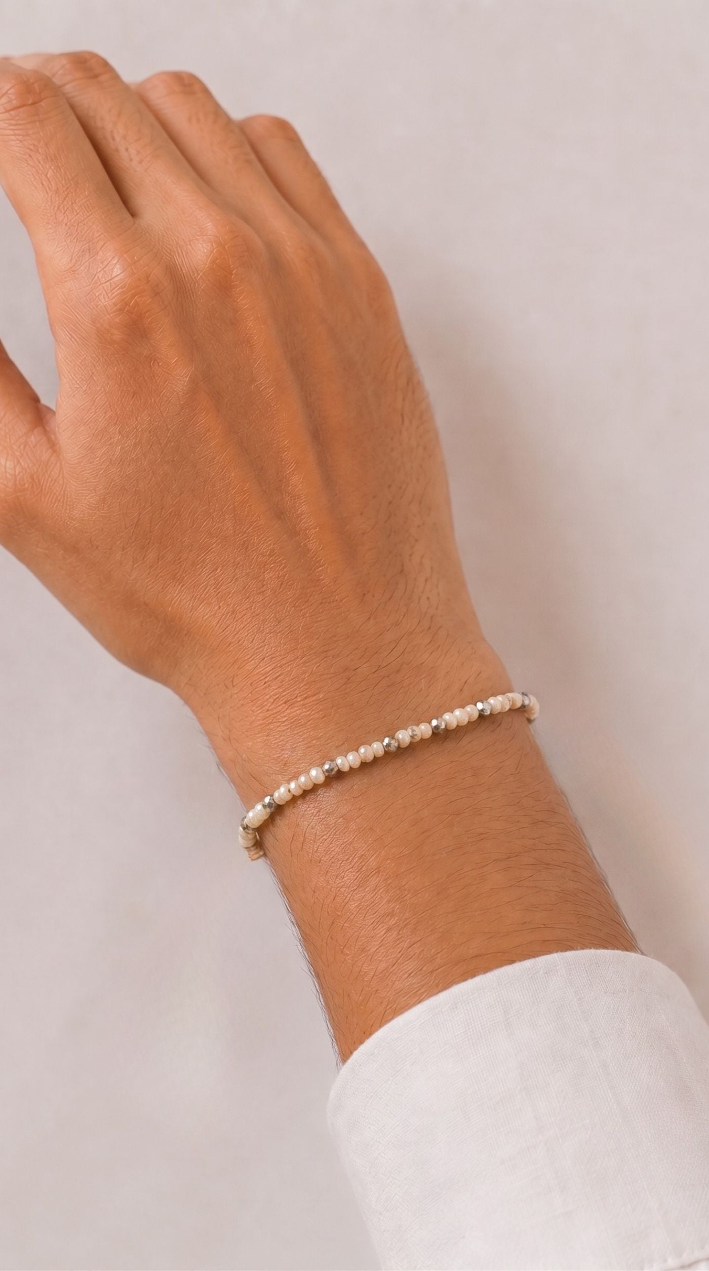 Minimal white pearl beaded rakhi bracelet with silver-tone spacer beads worn on a man's wrist – Diya Online