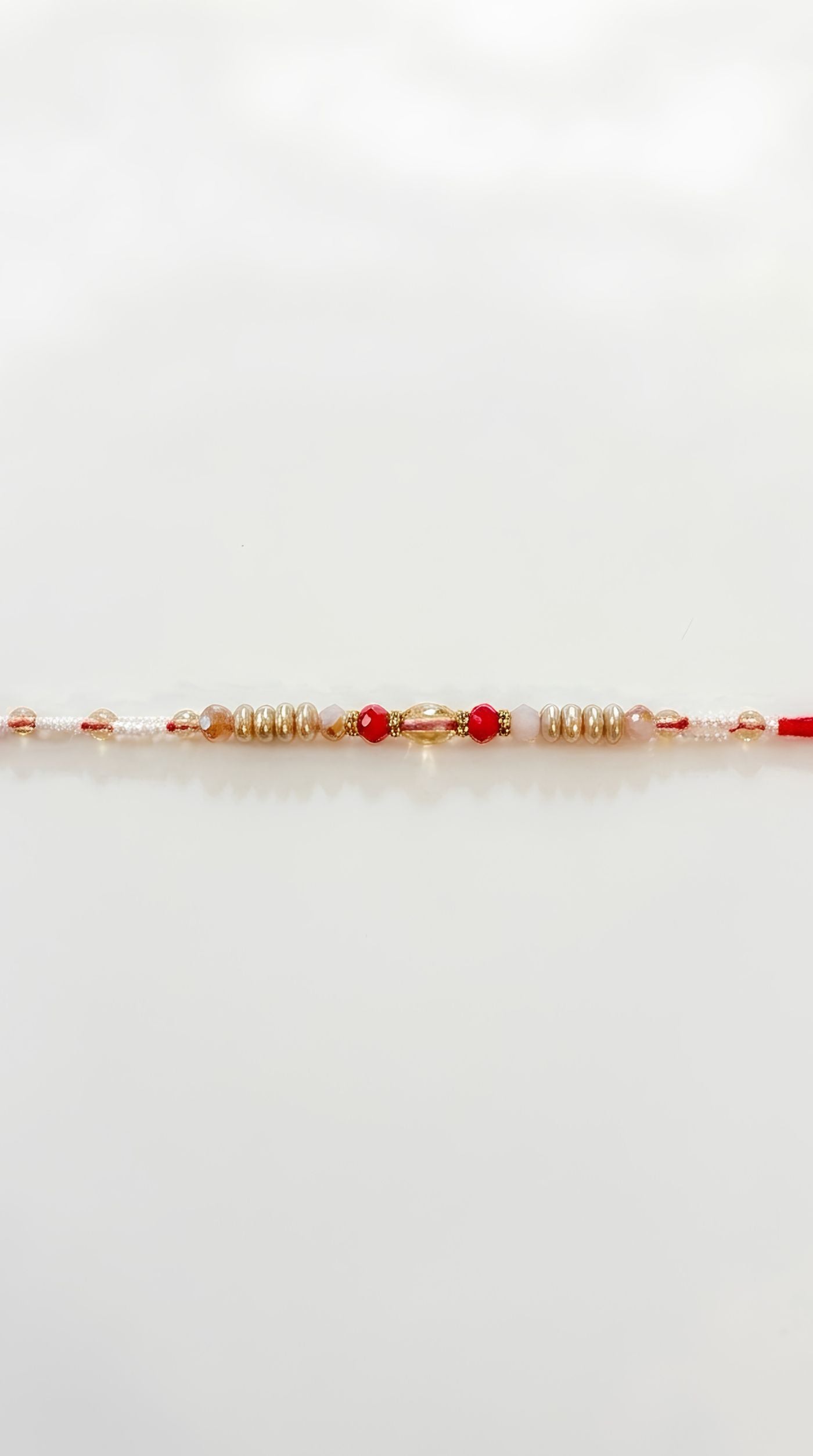 Pearl and crystal beaded rakhi bracelet with red accent beads and gold-tone spacers worn on a man's wrist – Diya Online