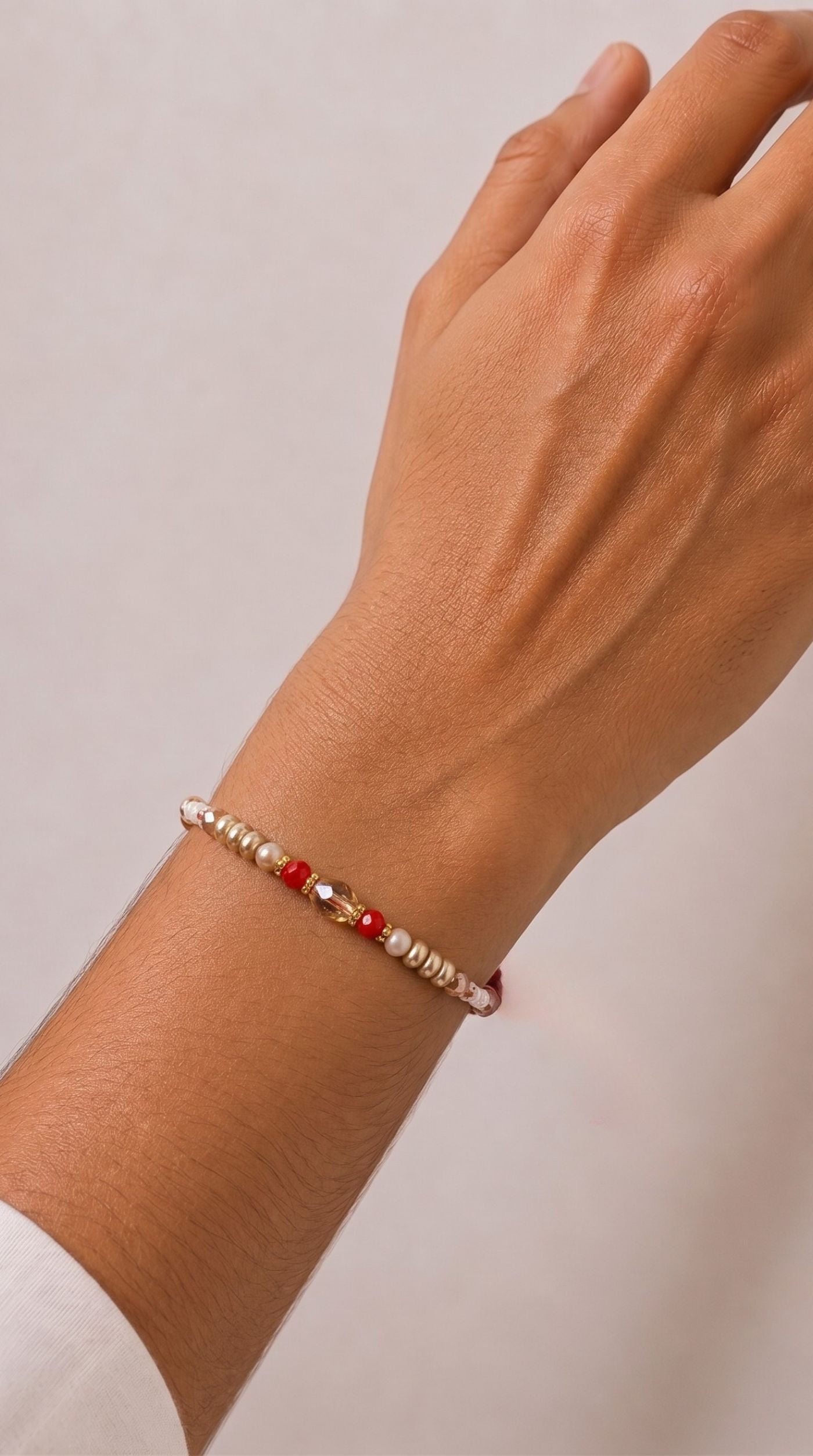 Pearl and crystal beaded rakhi bracelet with red accent beads and gold-tone spacers worn on a man's wrist – Diya Online