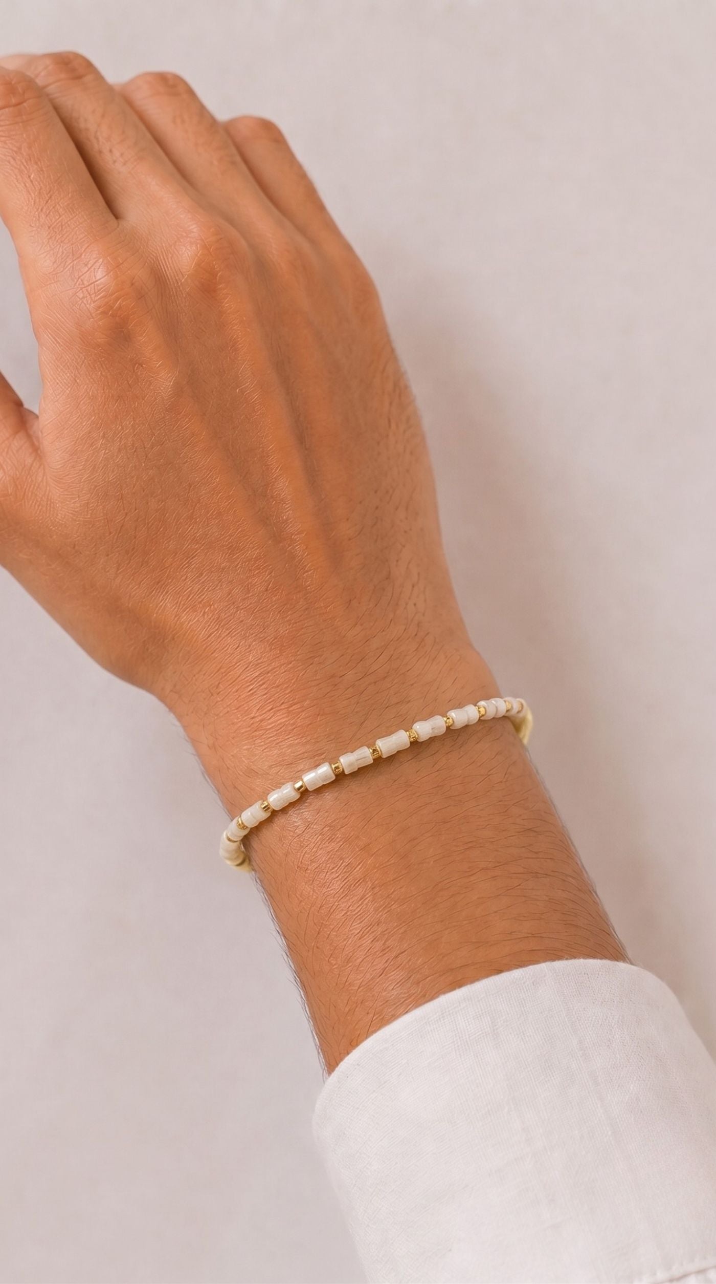 Minimal white beaded rakhi bracelet with gold-tone spacer beads worn on a man's wrist – Diya Online