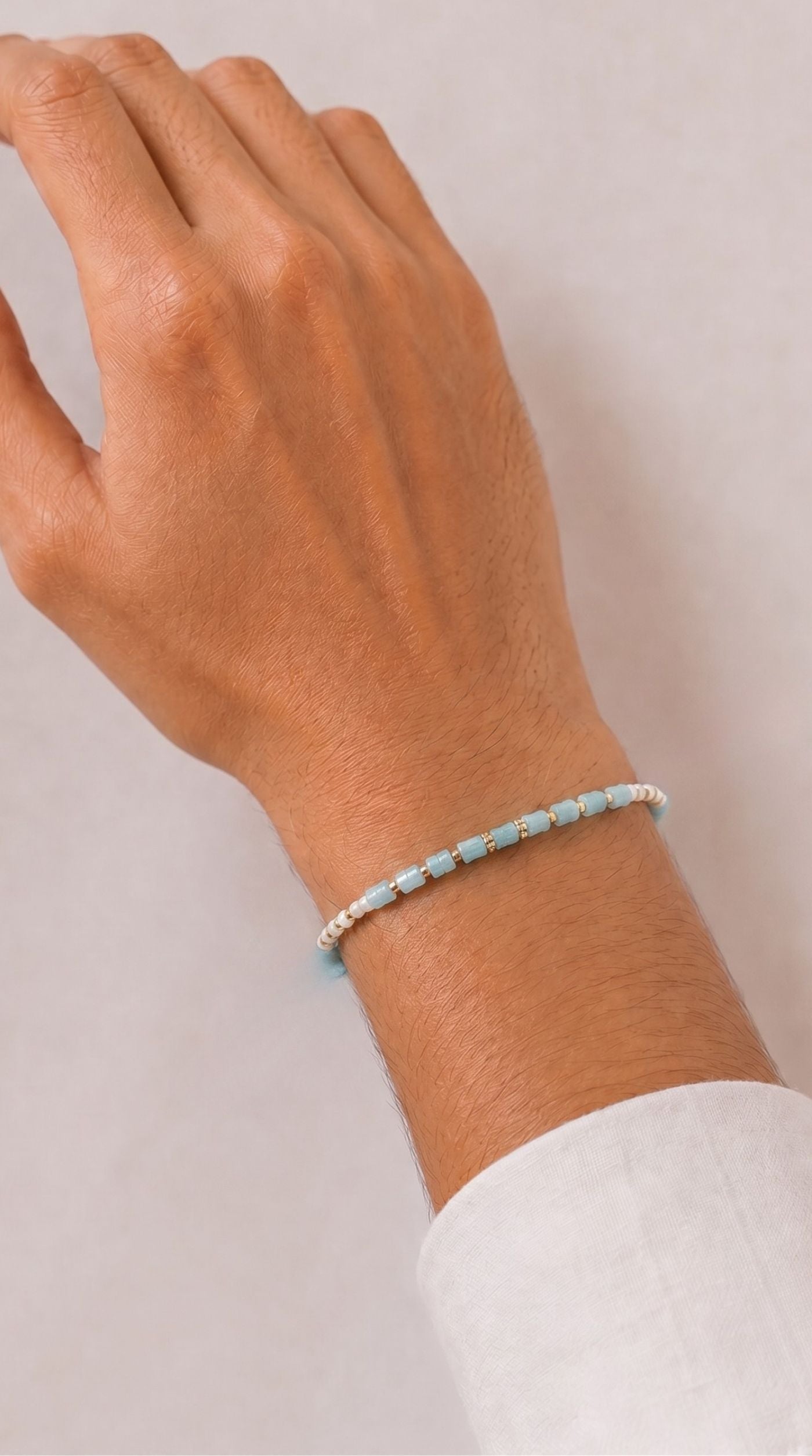 Minimal blue and white beaded rakhi bracelet with gold-tone spacer beads worn on a man's wrist – Diya Online