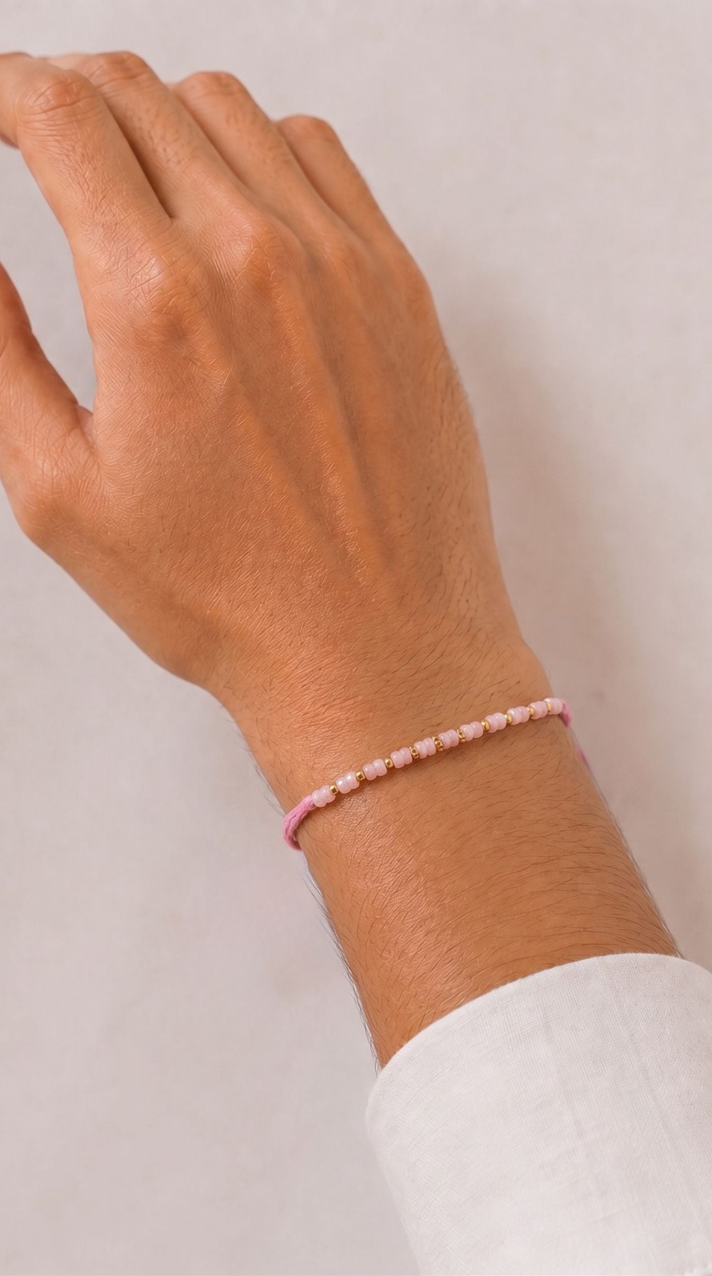 Minimal pink beaded rakhi bracelet with gold-tone spacer beads and matching pink thread worn on a man's wrist – Diya Online