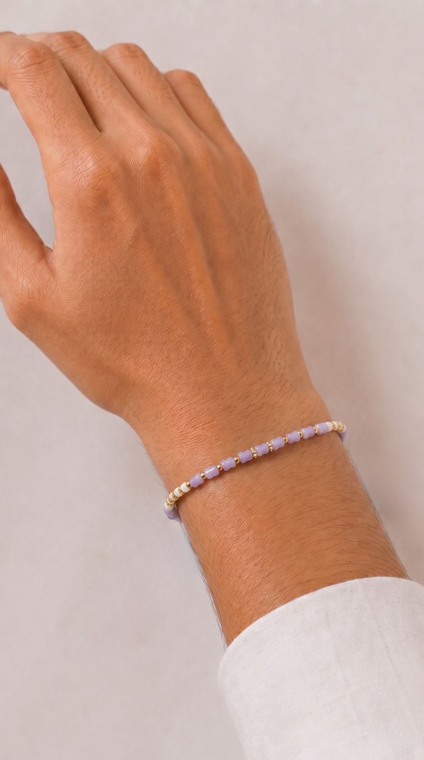 Minimal lavender beaded rakhi bracelet with gold-tone spacer beads and adjustable thread worn on a man's wrist – Diya Online