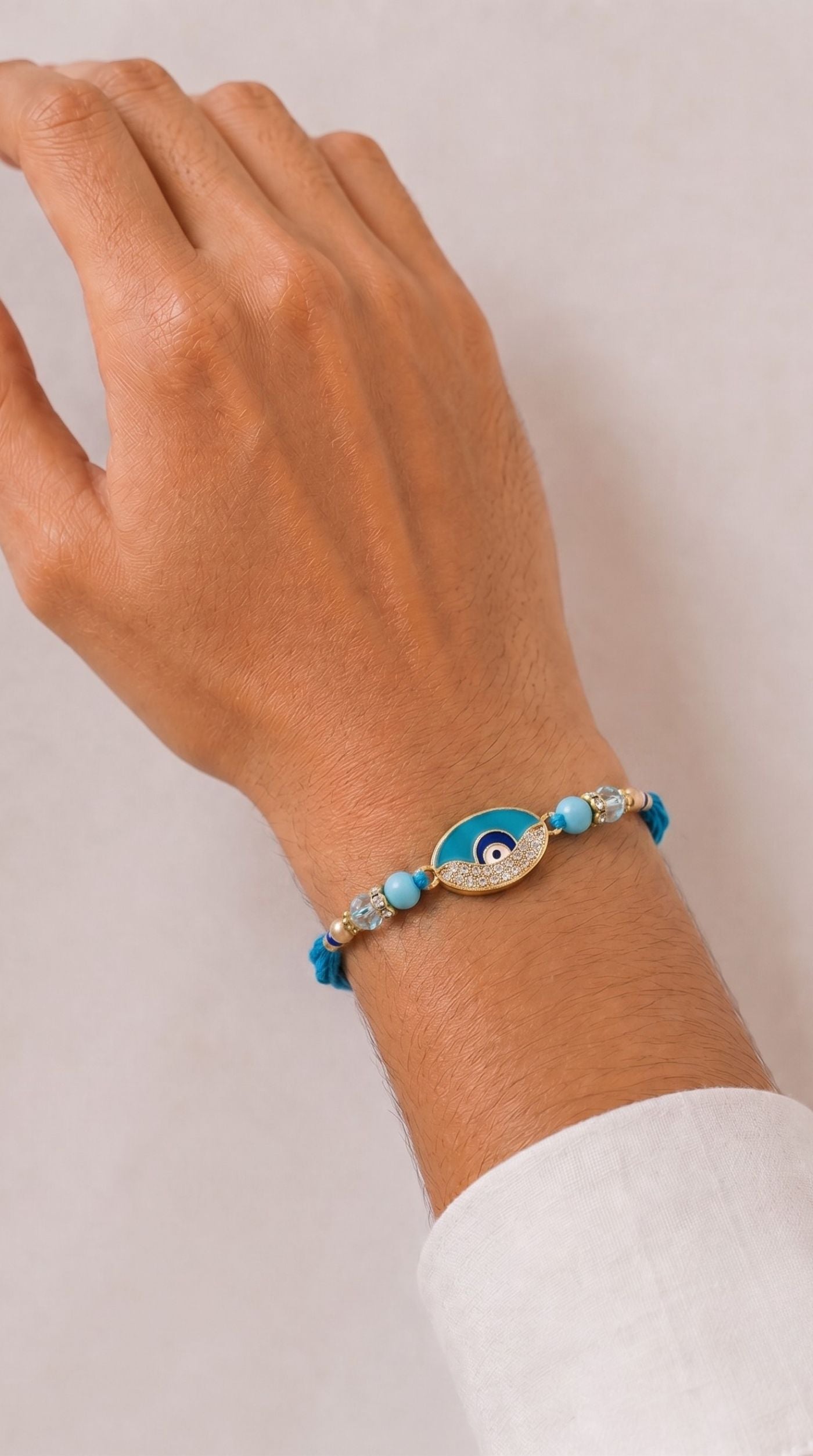 Blue evil eye rakhi bracelet with crystal detailing, blue beads, and adjustable blue thread worn on a man's wrist – Diya Online
