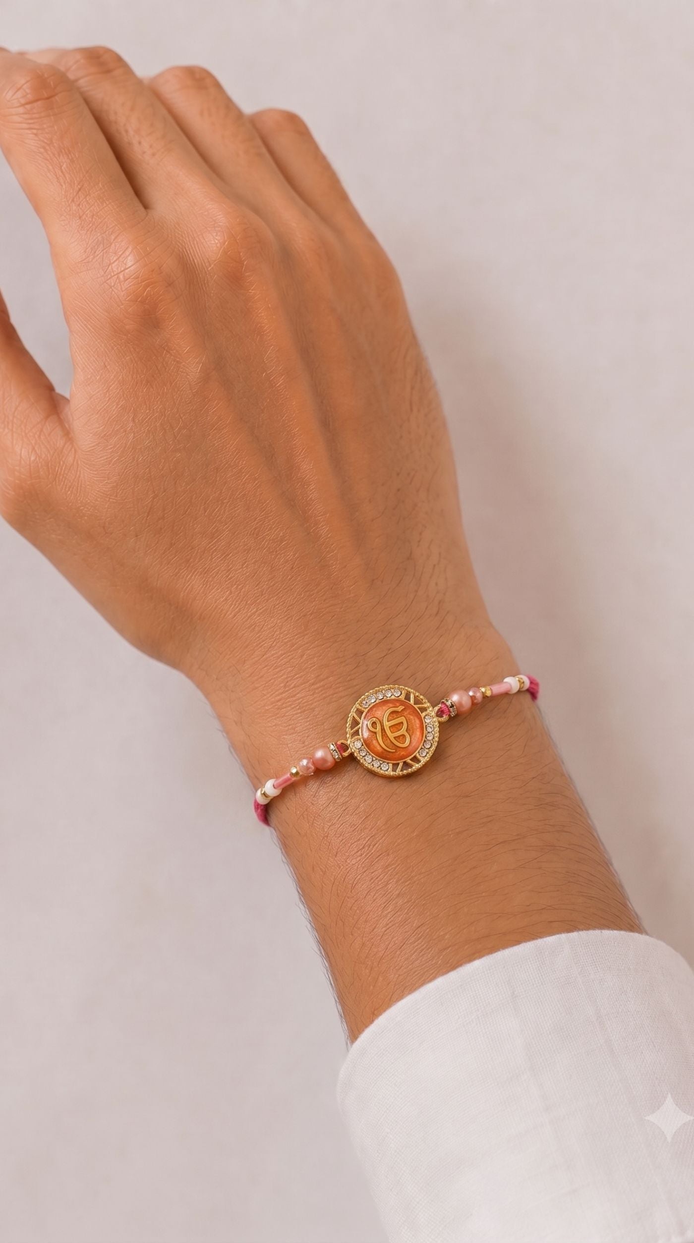Ek Onkar rakhi bracelet with crystal-studded gold-tone Ek Onkar charm, pink pearl beads, white seed beads, and adjustable pink thread worn on a man's wrist – Diya Online