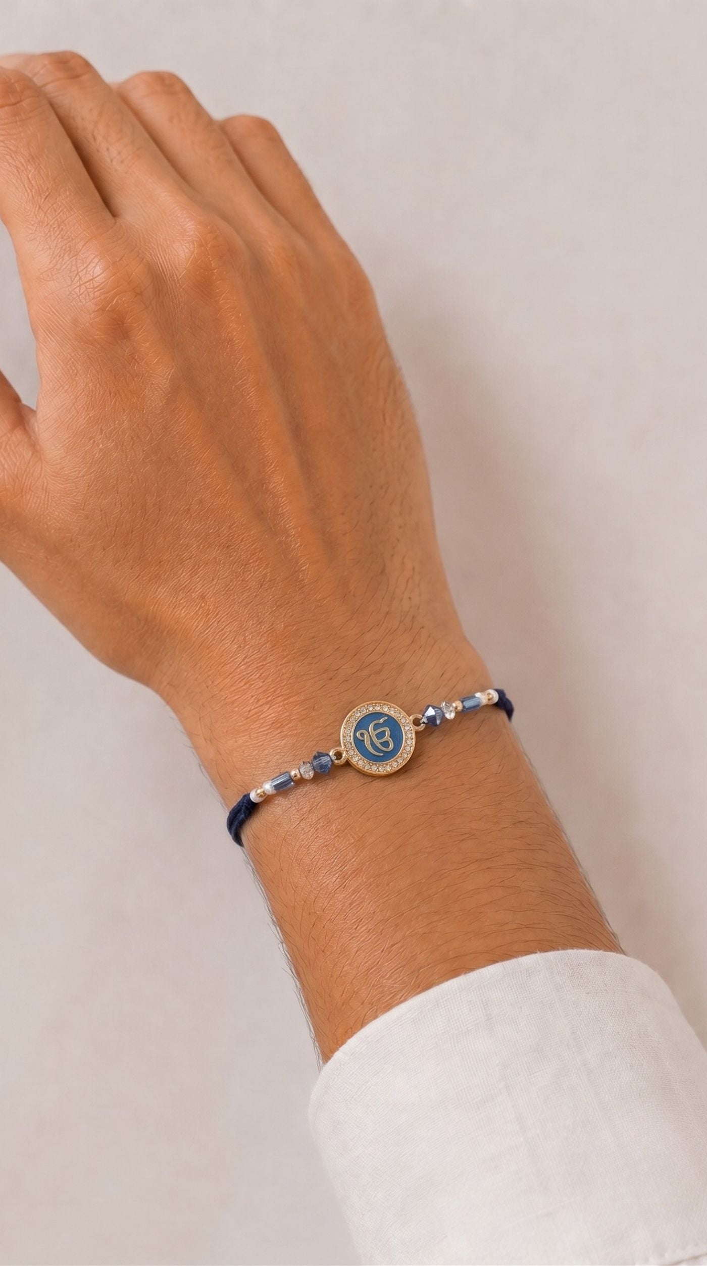 Blue Ek Onkar rakhi bracelet with crystal-studded centerpiece, blue crystal beads, silver-tone spacers, and adjustable navy thread worn on a man's wrist – Diya Online